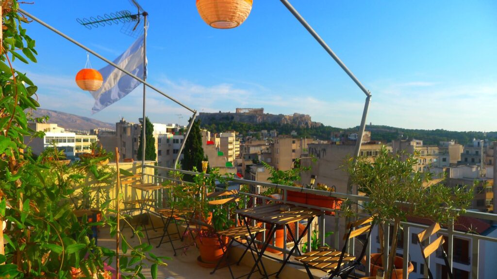Πρωινή θέα της Ακρόπολης από μπαλκόνι. Στο μπαλκόνι υπάρχουν φυτά, τραπεζάκια και μια σημαία της Αργεντινής.