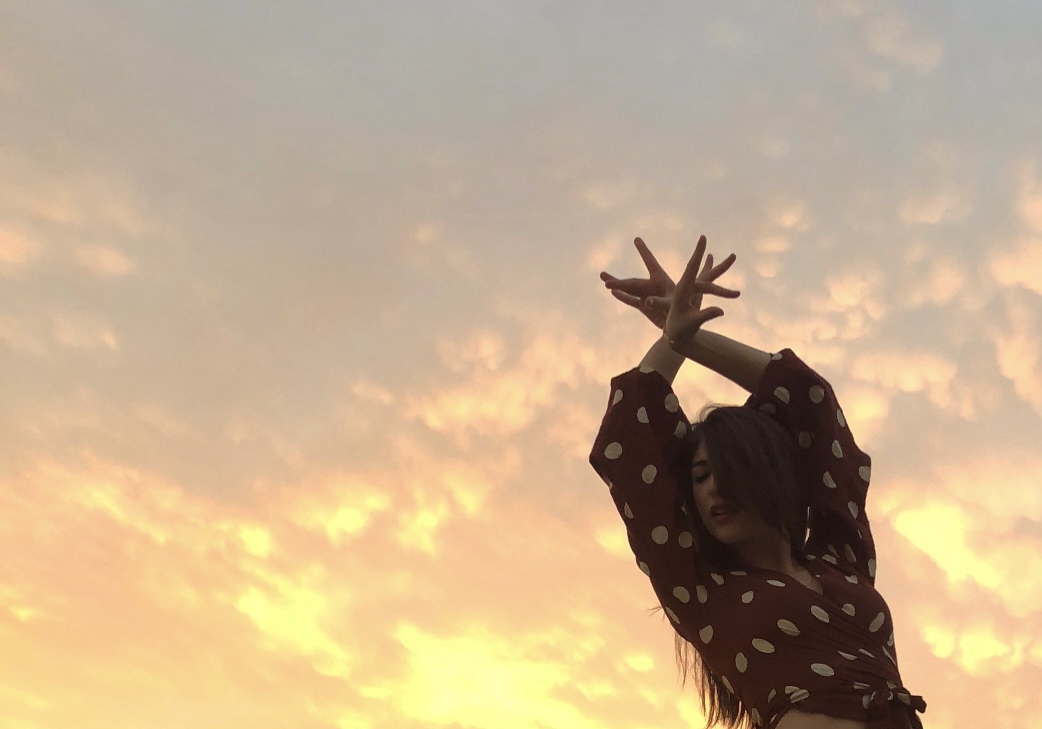 Φωτογραφία της Βάσια Κατσιγιάννη που κάνει μια κίνηση flamenco με τα χέρια της. Βλέπουμε μόνο το πάνω μέρος του σώματός της και φόντο είναι ο ουρανός.