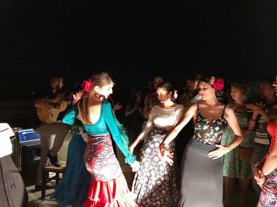 Μια παρέα γυναικών με λουλουδάτες φούστες και φορέματα χορεύουν flamenco σε ένα πάρτυ.