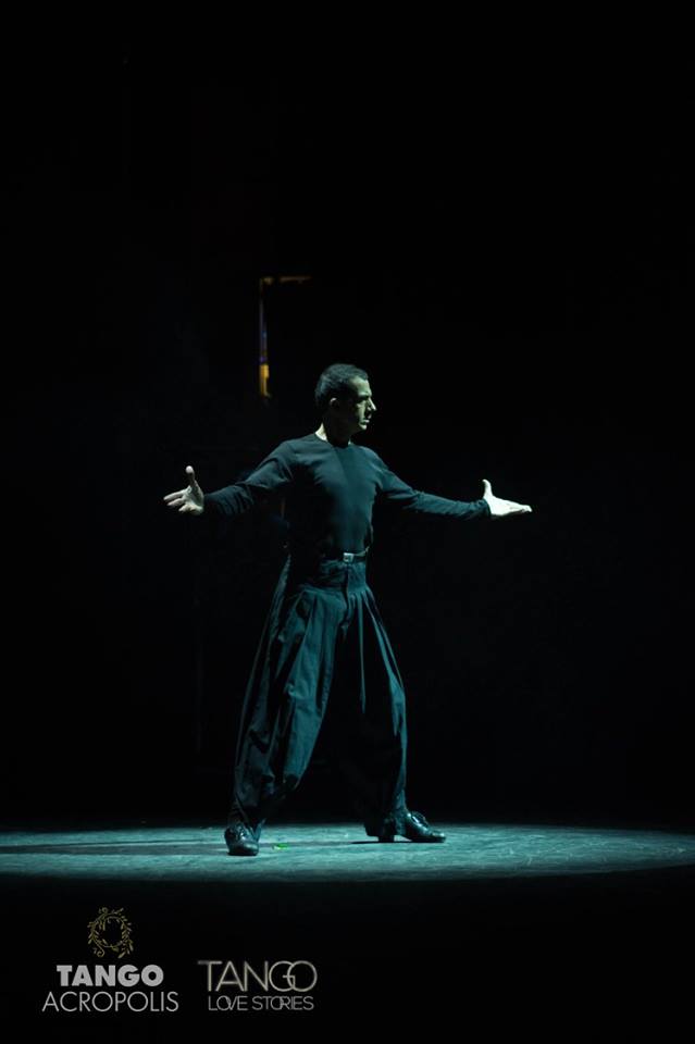 Ολόσωμη φωτογραφία του Ariel Perez σε μια δυναμική πόζα σε μια θεατρική σκηνή. Φοράει μάυρα ρούχα και παπούτσια με τακούνια.