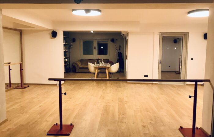 φωτογραφία από το εσωτερικό του Tango Atelier Home όπου φαίνεται ένας μεγάλος χωρος με ξύλινο πάτωμα, καθρέφτη και μπάρες στήριξης. Στο βάθος φαίνεται ένα μικρό καθιστικό.