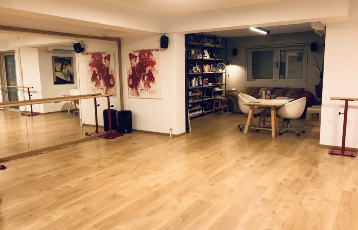 φωτογραφία από το εσωτερικό του Tango Atelier Home όπου φαίνεται ένας μεγάλος χωρος με ξύλινο πάτωμα, καθρέφτη και μπάρες στήριξης. Στο βάθος φαίνεται ένα μικρό καθιστικό.